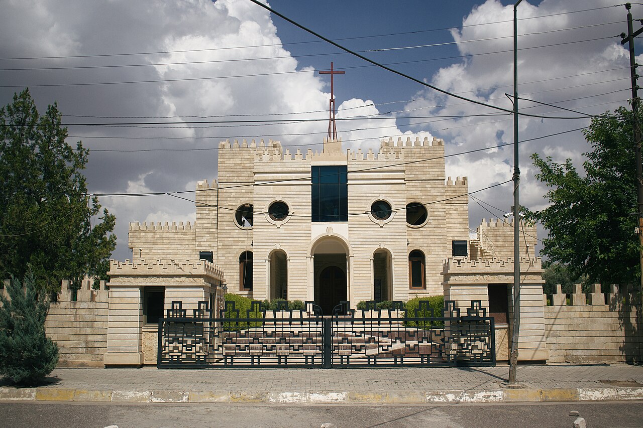 Saint Joseph’s Chaldean Catholic church in Ankawa, with a cross, pale stone façade, circular windows and patterned metal gate