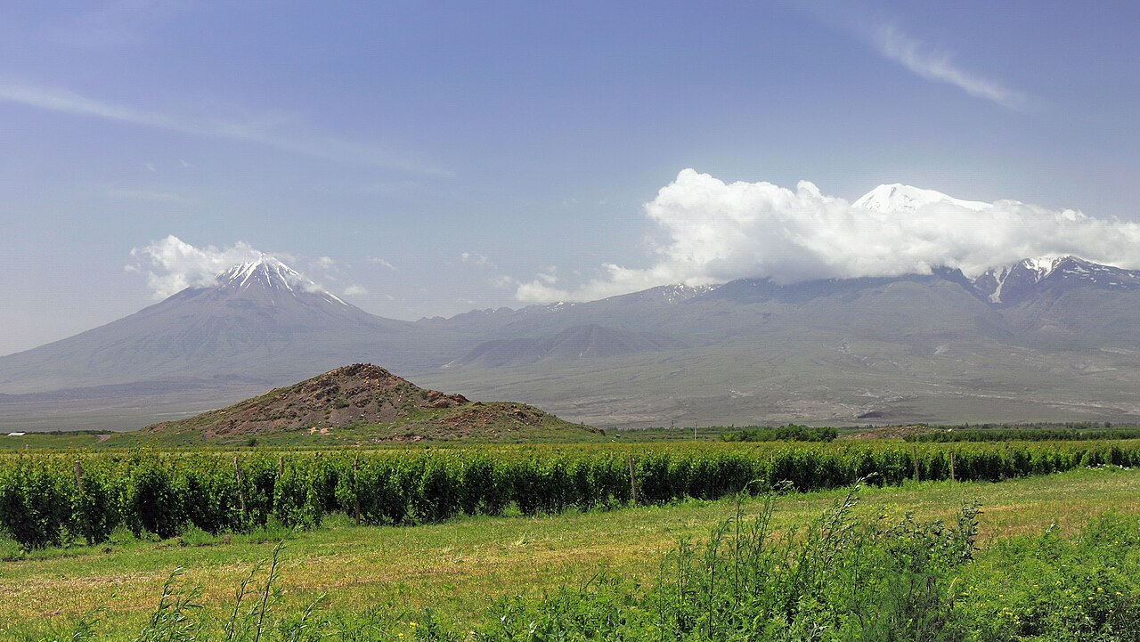 Little Ararat on the left and cloud-covered, snow-capped Great Ararat on the right beyond green fields, viewed from Armenia