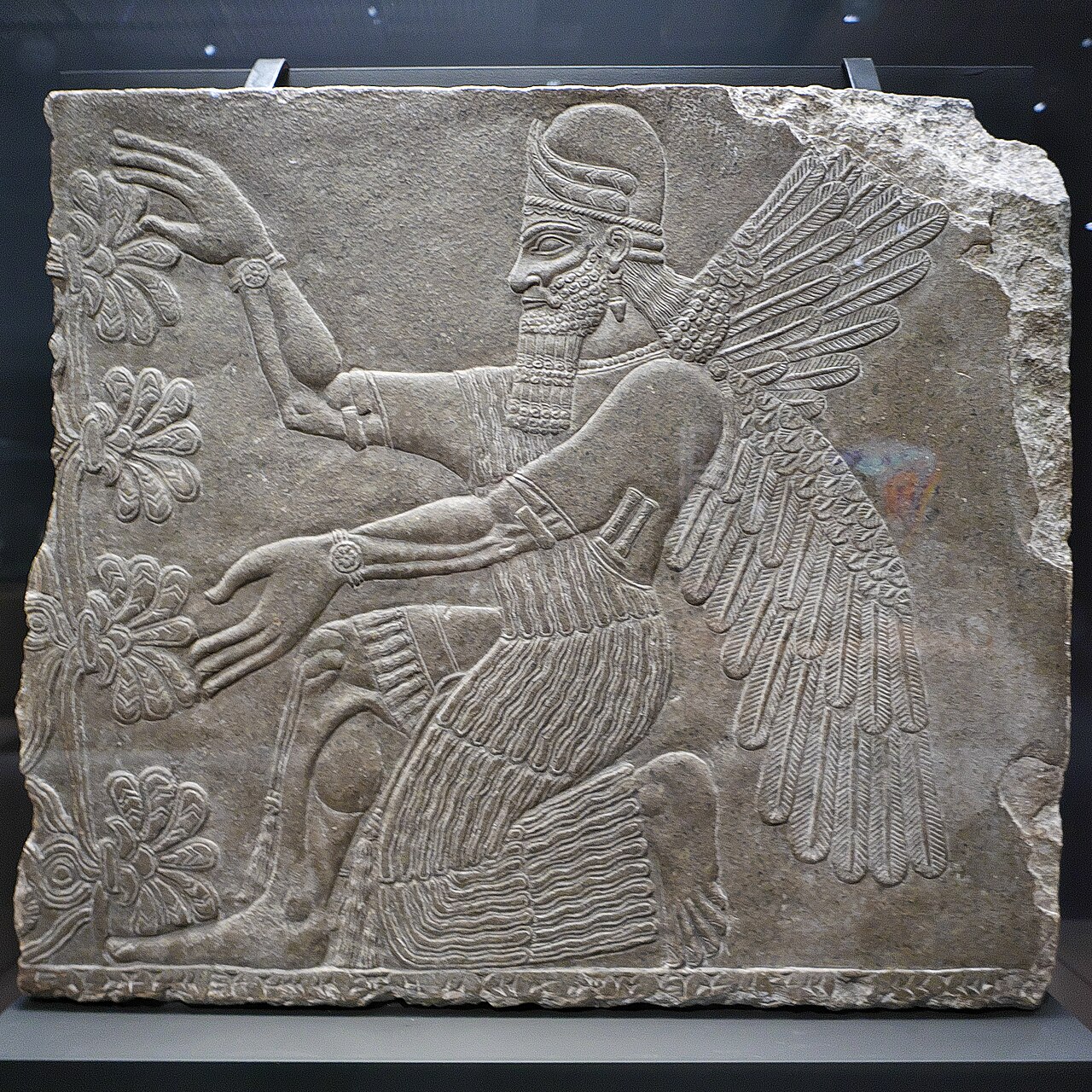 Assyrisk stenrelief från Nimrud med en skäggig bevingad figur på knä intill ett stiliserat träd