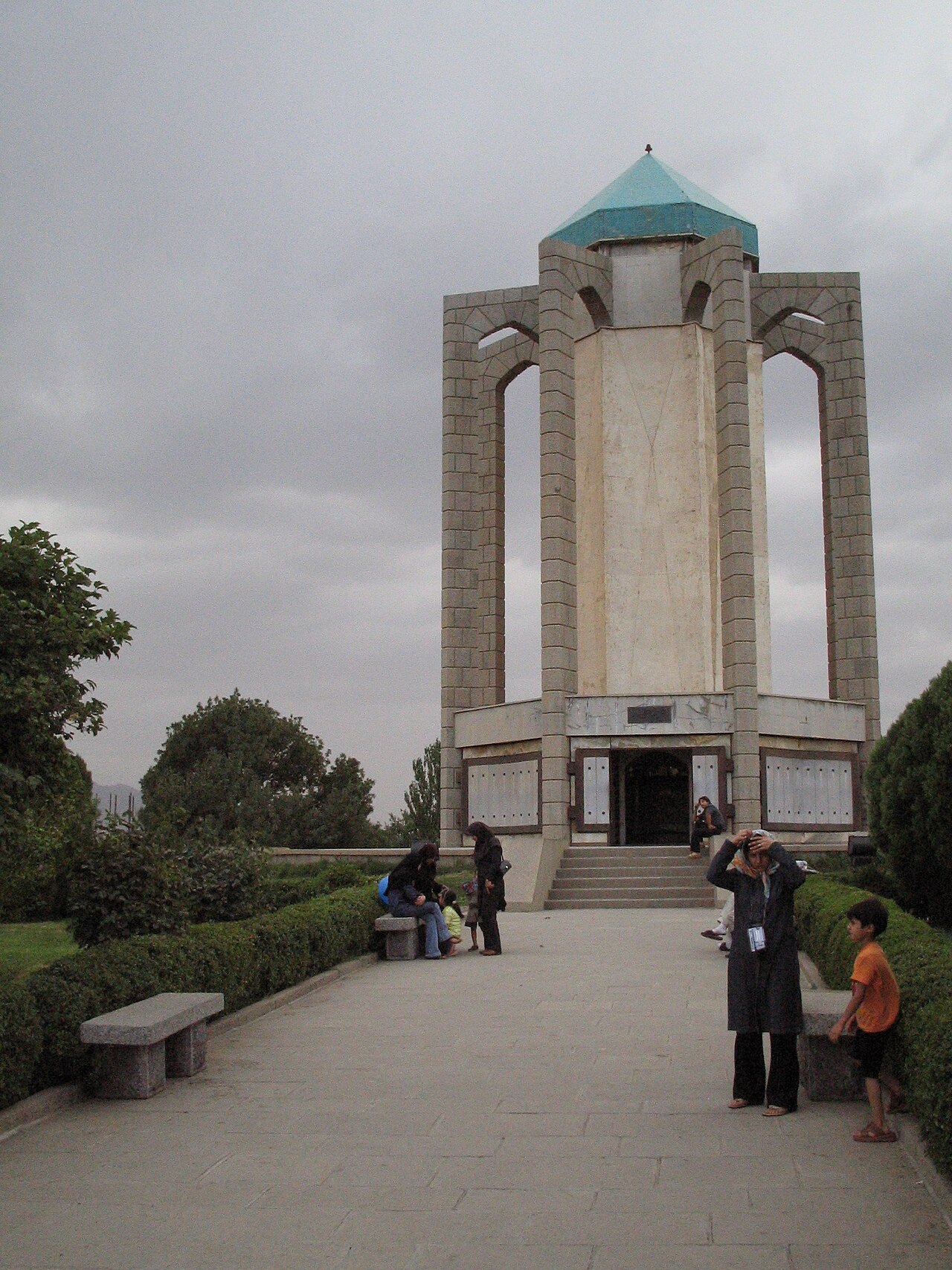 Visitors outside Baba Tahir’s stone mausoleum in Hamadan, with tall open arches and a turquoise roof