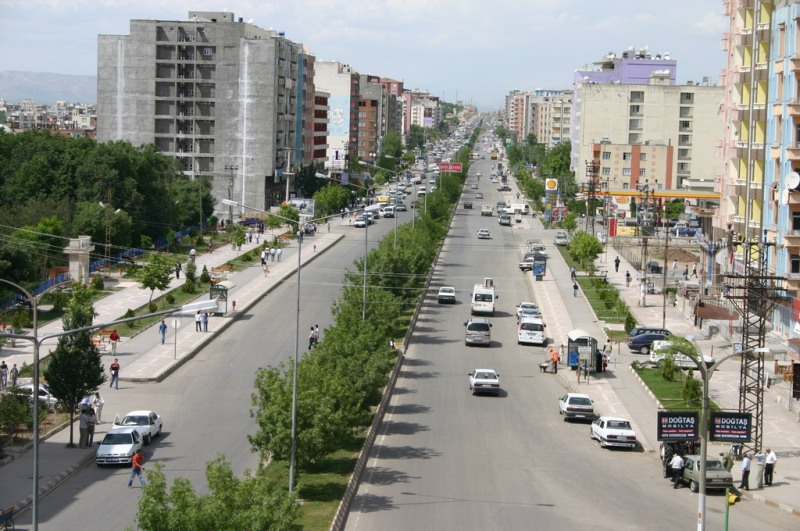 Elevated view along a broad divided boulevard in Batman, with a planted median, traffic, pedestrians and apartment buildings