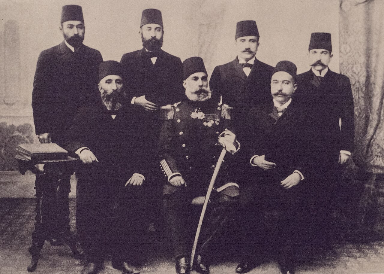 سبعة من أفراد عائلة بدرخان يرتدون الطرابيش؛ ثلاثة جالسون وأربعة واقفون، والجالس في الوسط بزي عسكري مزين بالأوسمة
