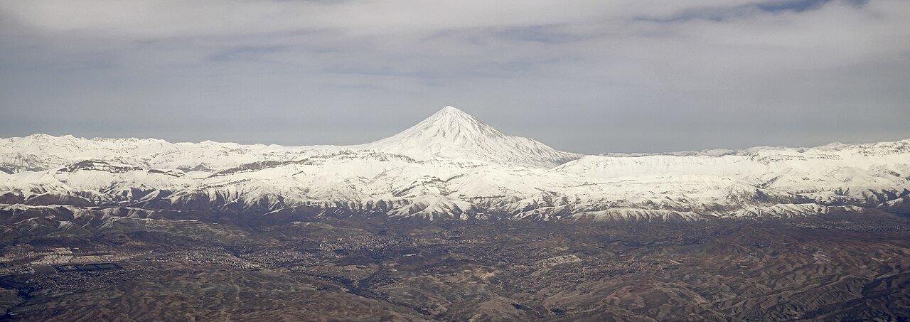Besneeuwde Damavand boven een brede bergketen en bruine uitlopers in een luchtpanorama
