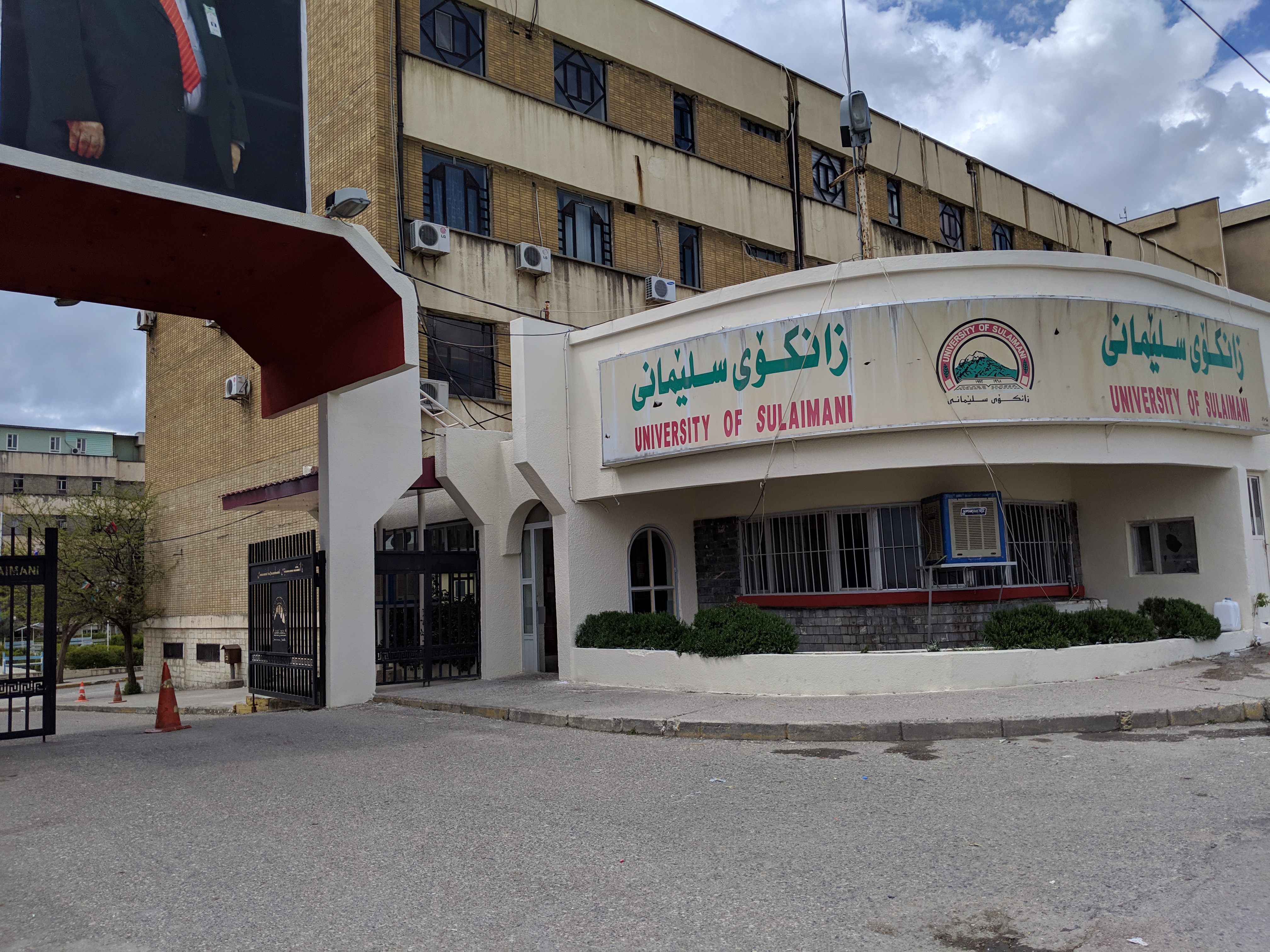 The old University of Sulaimani campus entrance with Kurdish and English signs below a multistorey building