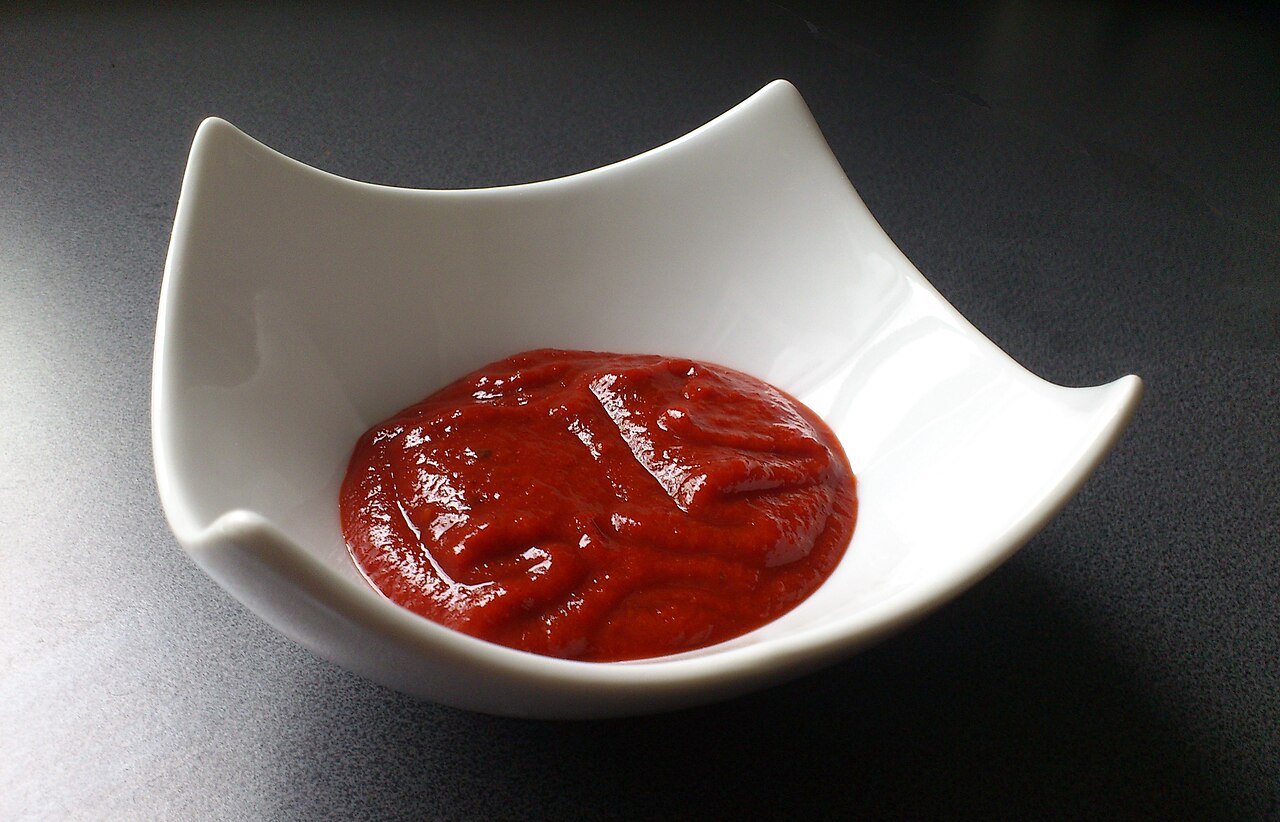 Thick glossy red pepper paste in a white bowl with four raised corners, on a dark kitchen surface