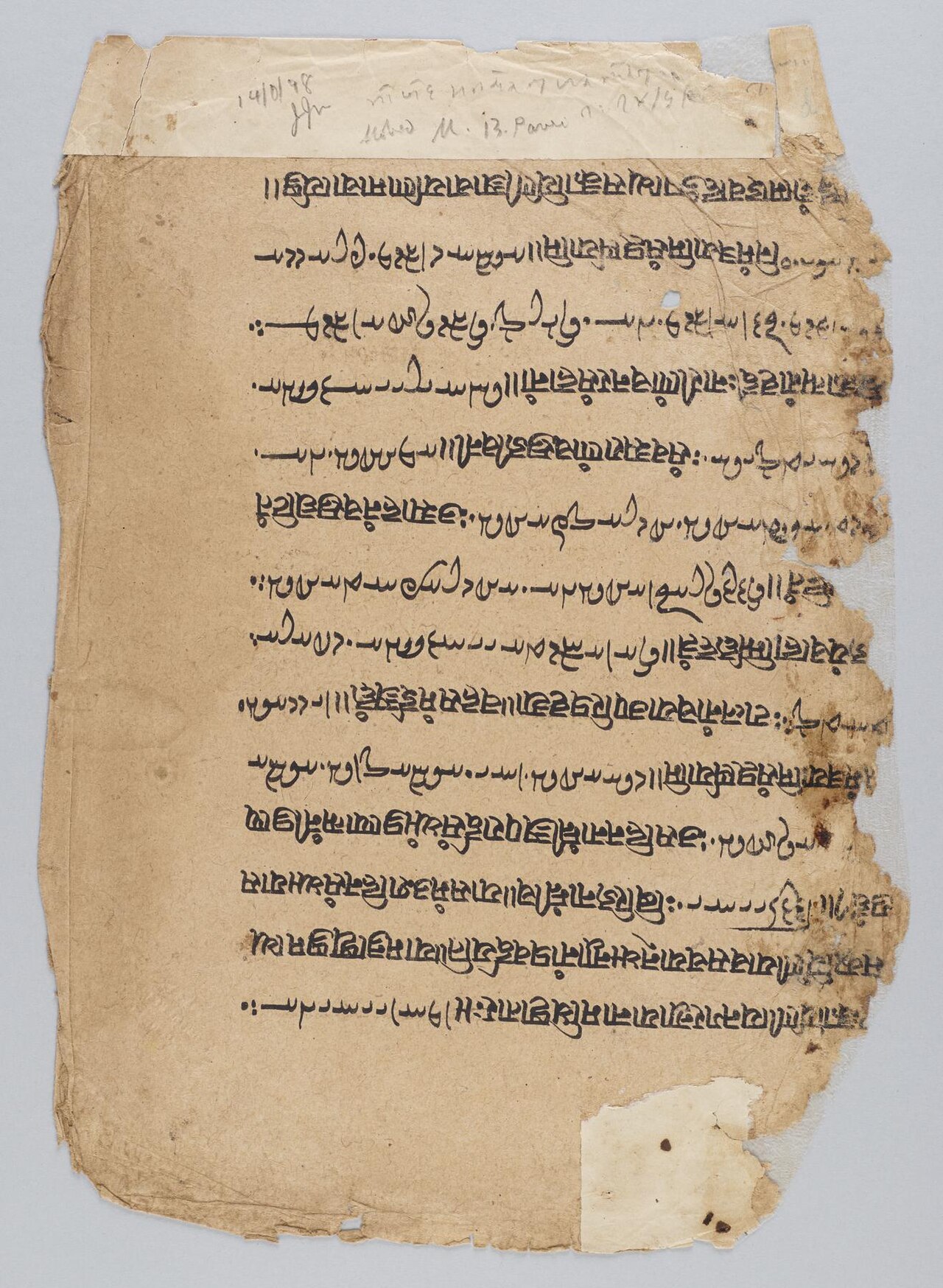 A worn manuscript leaf with alternating lines of Avestan and Sanskrit writing, torn edges and handwritten annotations along the top