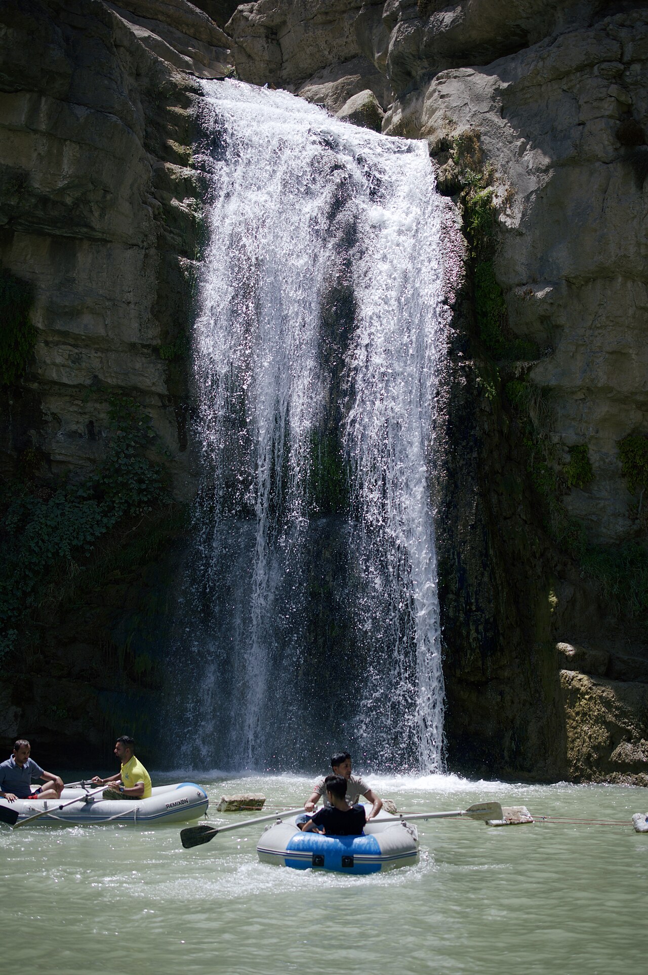 White water drops between dark rock walls at Gali Ali Beg while visitors row inflatable boats in the pool below