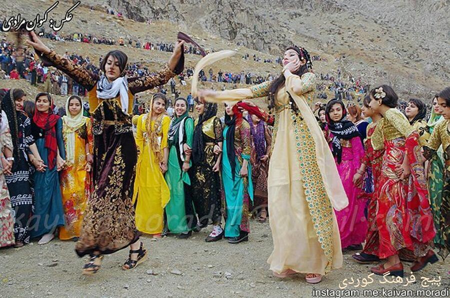 Women in colourful dresses dance with scarves before a linked line of dancers in Hawraman