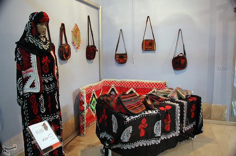 Etalagepop met zwart-rood-wit gedessineerde hoofddoek en jurk naast stoffen en gestreepte tassen aan een witte tentoonstellingswand