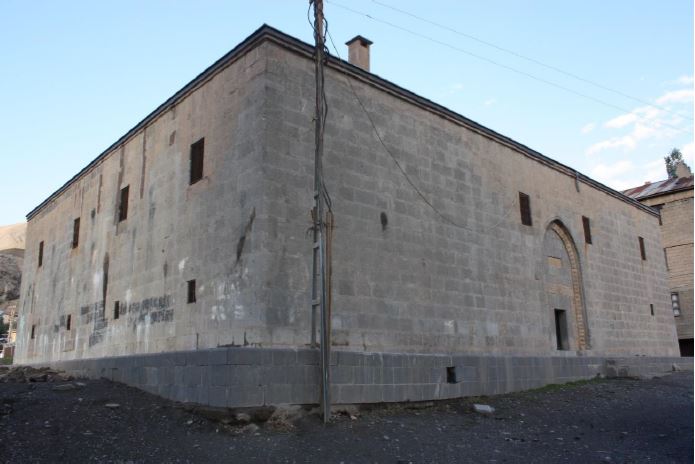 Two-storey stone exterior of the Meydan Medrese in Hakkari, with small windows and a tall pointed entrance arch