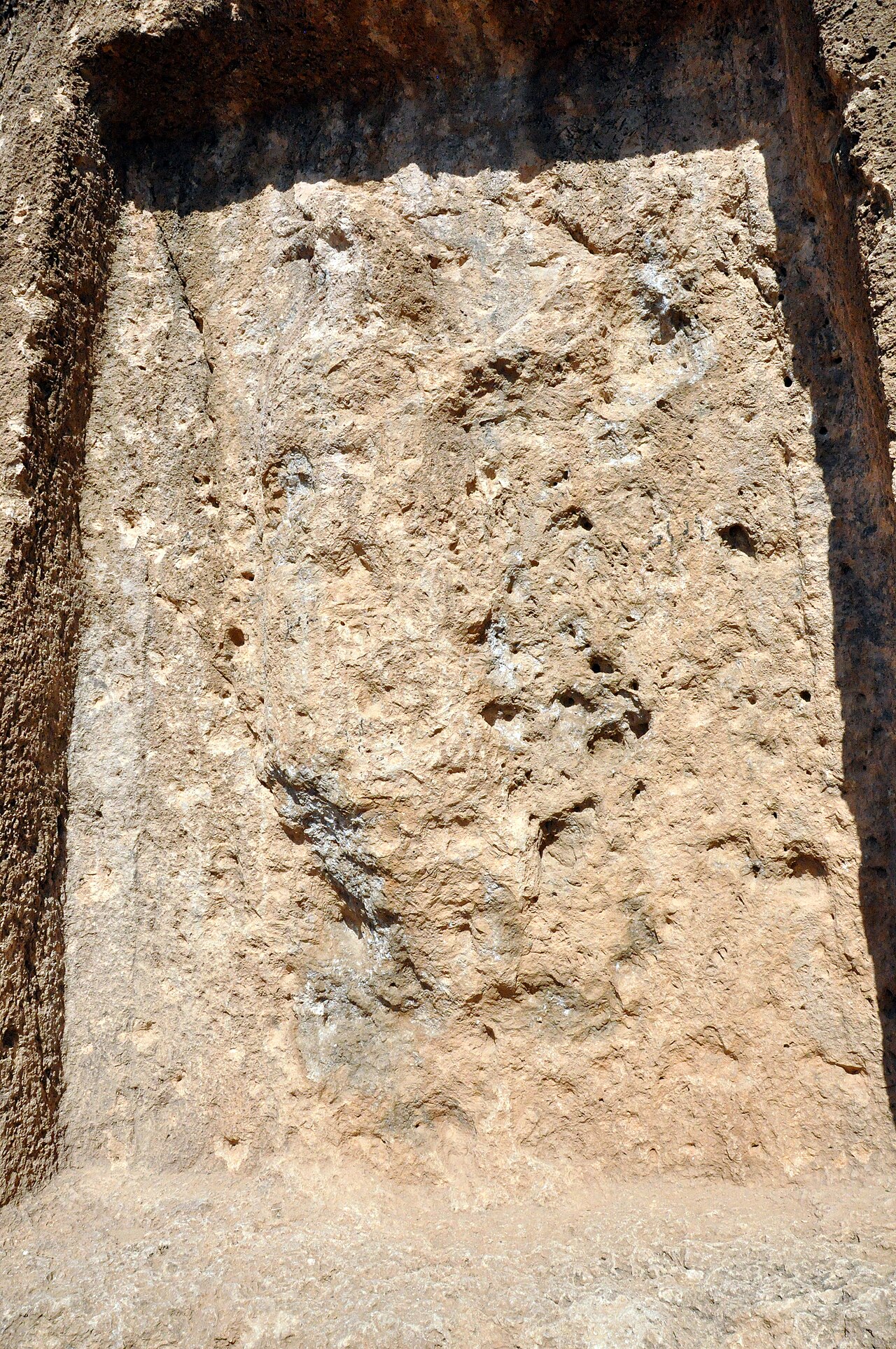 Heavily weathered standing human figure carved inside a rectangular rock-cut frame at Batas-Herir, with one arm raised