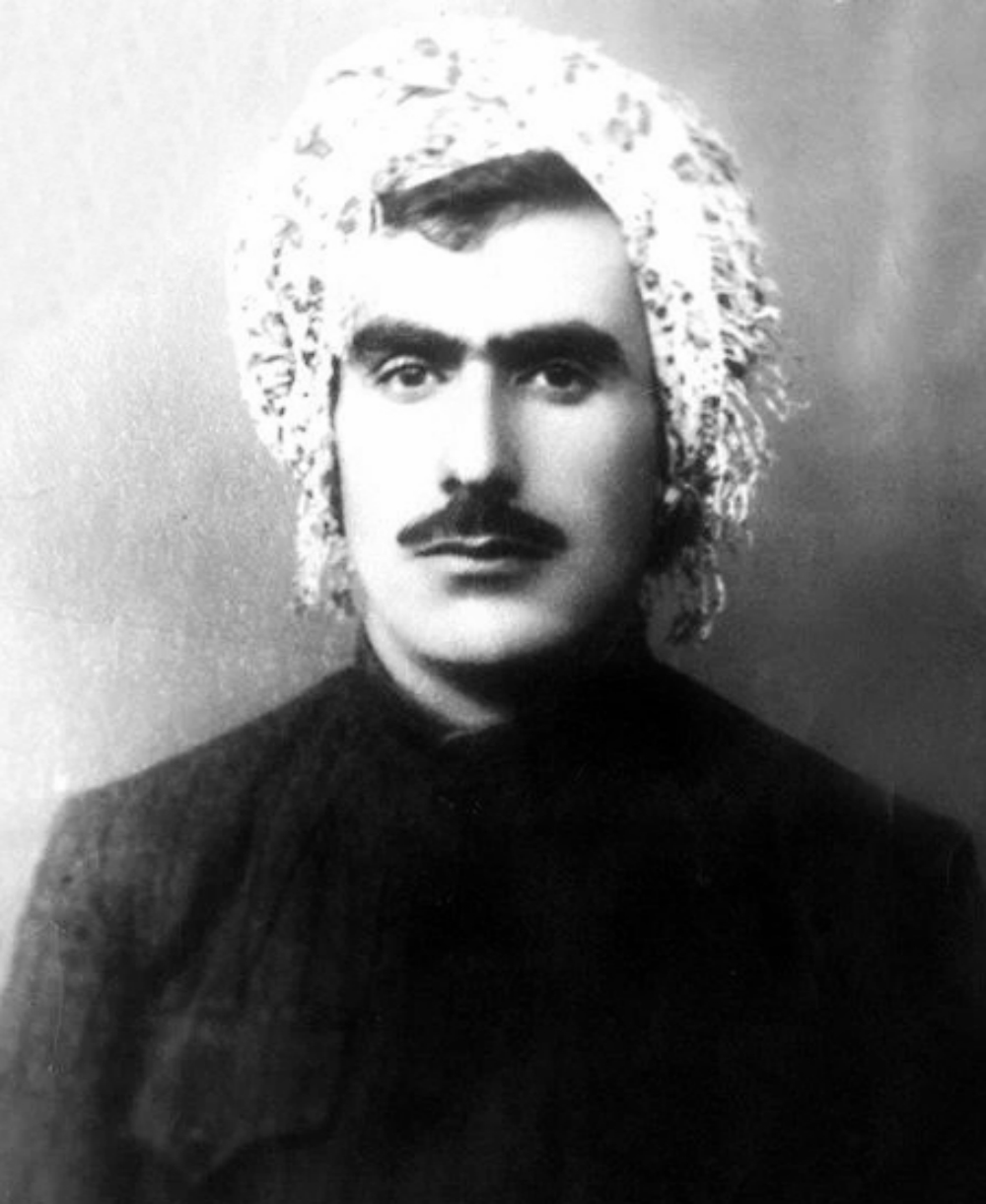 پرتره سیاه‌وسفید عبدالرحمان شرفکندی جوان با سبیل و سربند نقش‌دار و لباس سنتی تیره