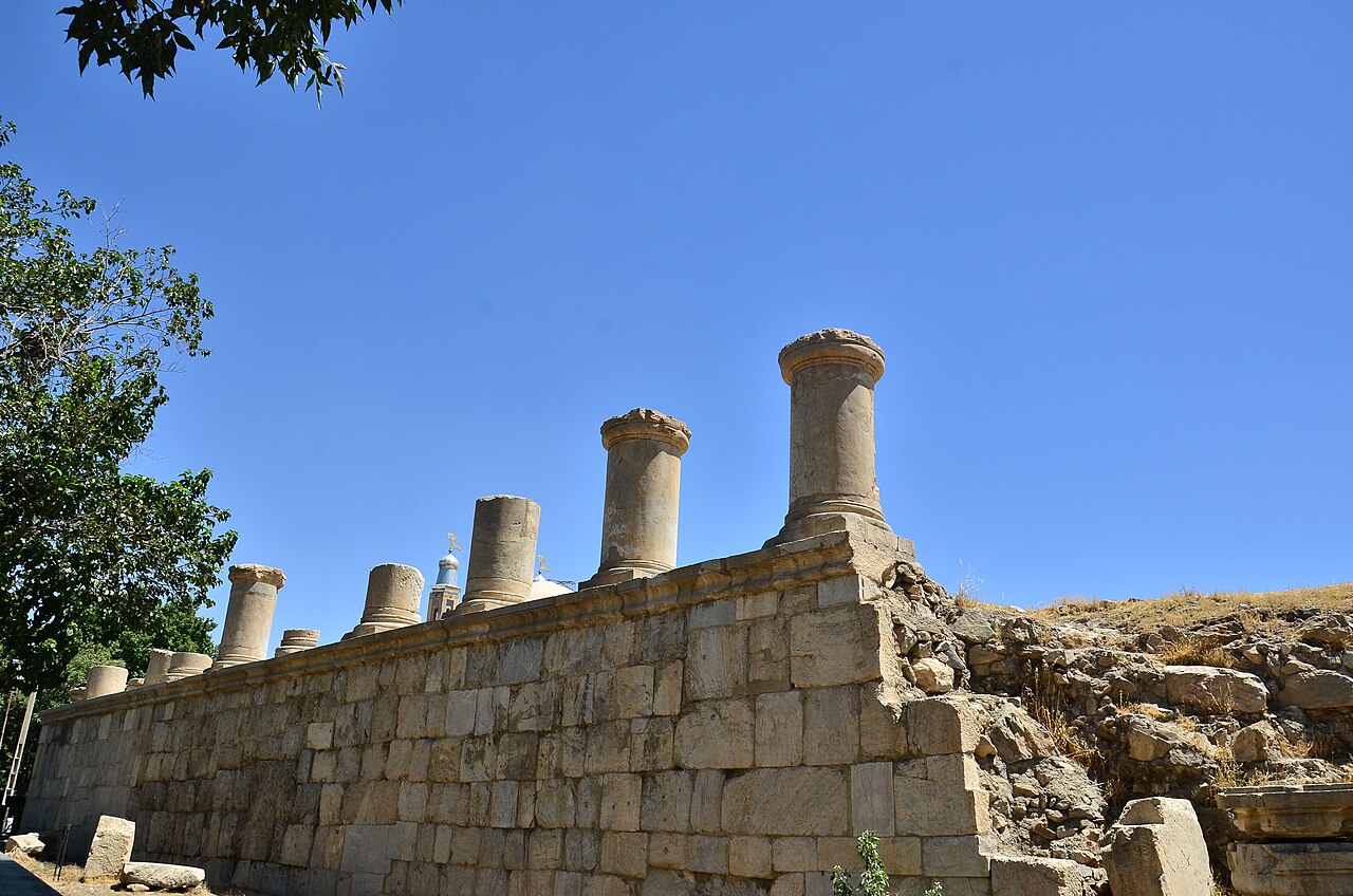 Short stone columns above a wall of large dressed blocks at Kangavar, beneath a clear blue sky