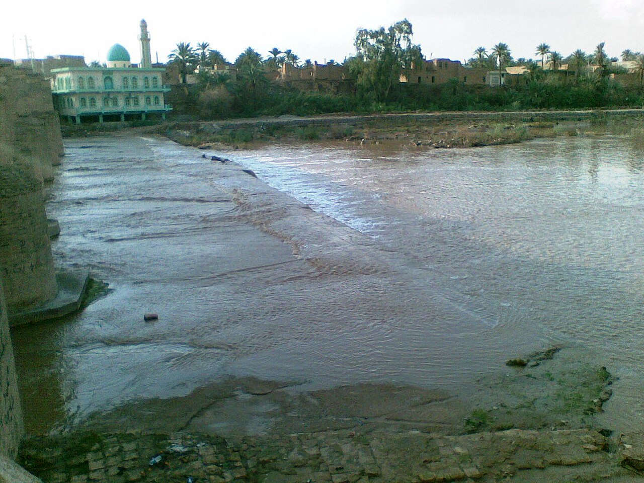 نهر الوند في خانقين مع دعامة جسر يساراً وأرض مكشوفة من مجرى النهر ومسجد ذي قبة خضراء على الضفة المقابلة