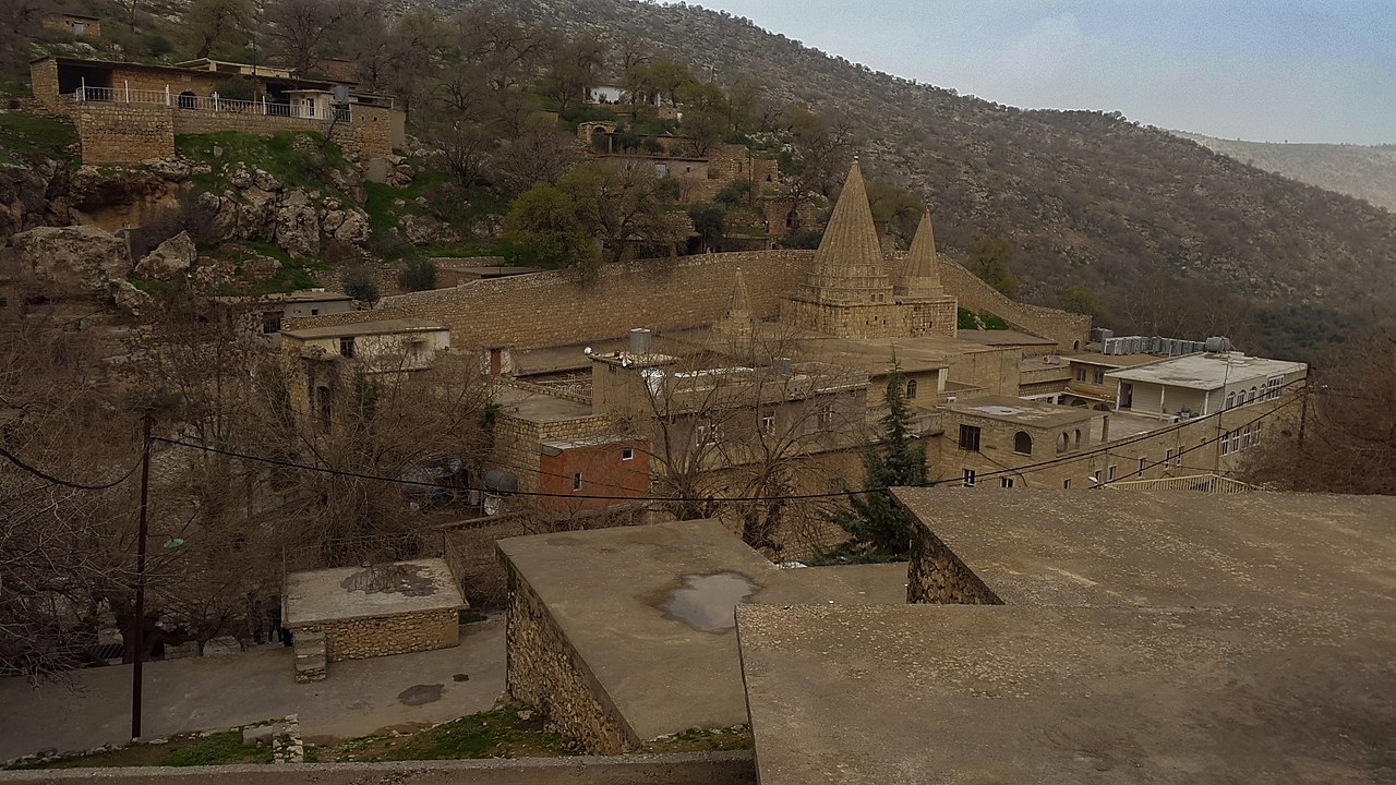 Stone buildings and two conical shrine roofs among trees in the valley of Lalish
