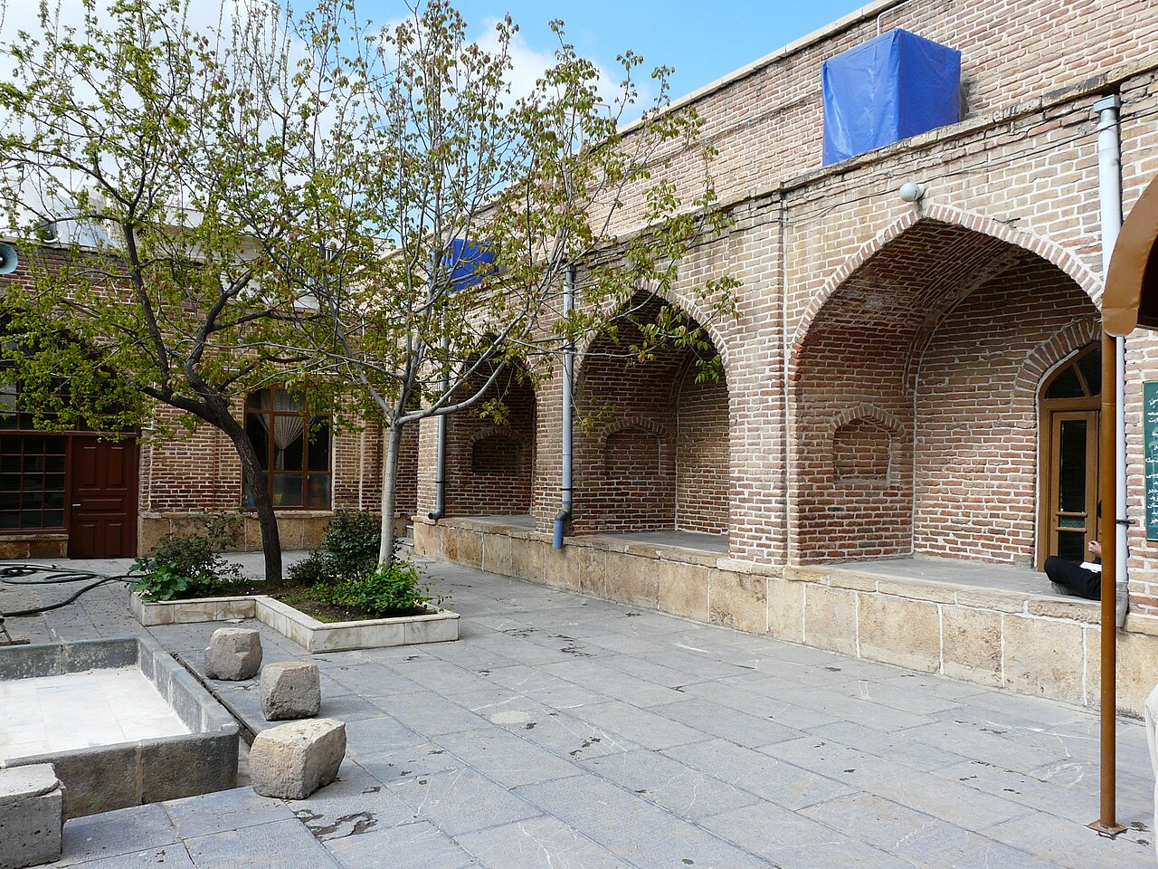 Pointed brick arches and doorways around the paved courtyard of Mahabad’s Red Mosque, with trees growing in rectangular stone beds