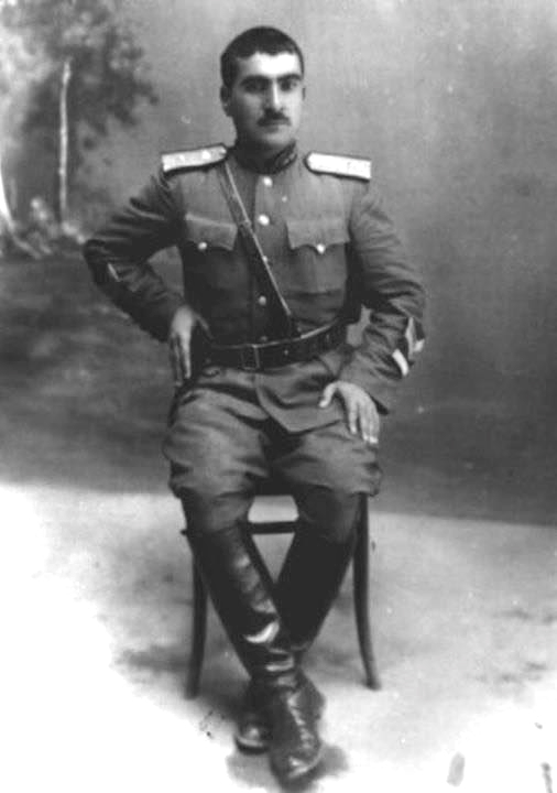 Mustafa Barzani’nin ahşap sandalyede apoletli ve kemerli askerî üniformayla oturduğu siyah beyaz stüdyo portresi