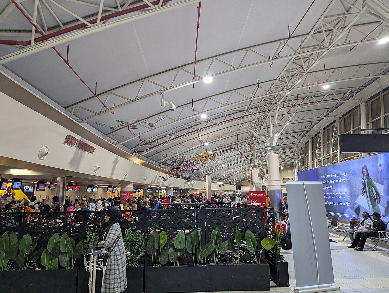 Passengers and check-in desks beneath the exposed roof trusses of a Jomo Kenyatta International Airport terminal
