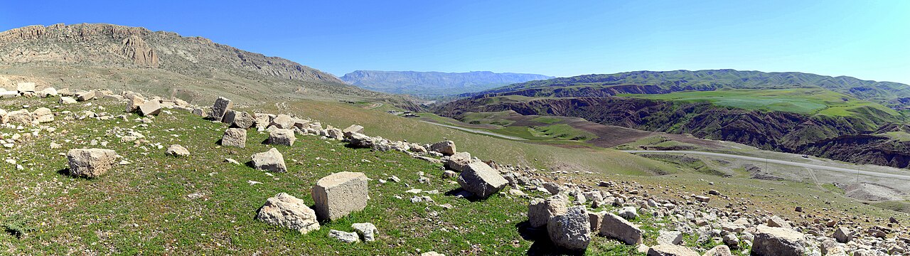 Scattered squared stone blocks at Paikuli on a green hillside overlooking a mountain valley, photographed in March 2015