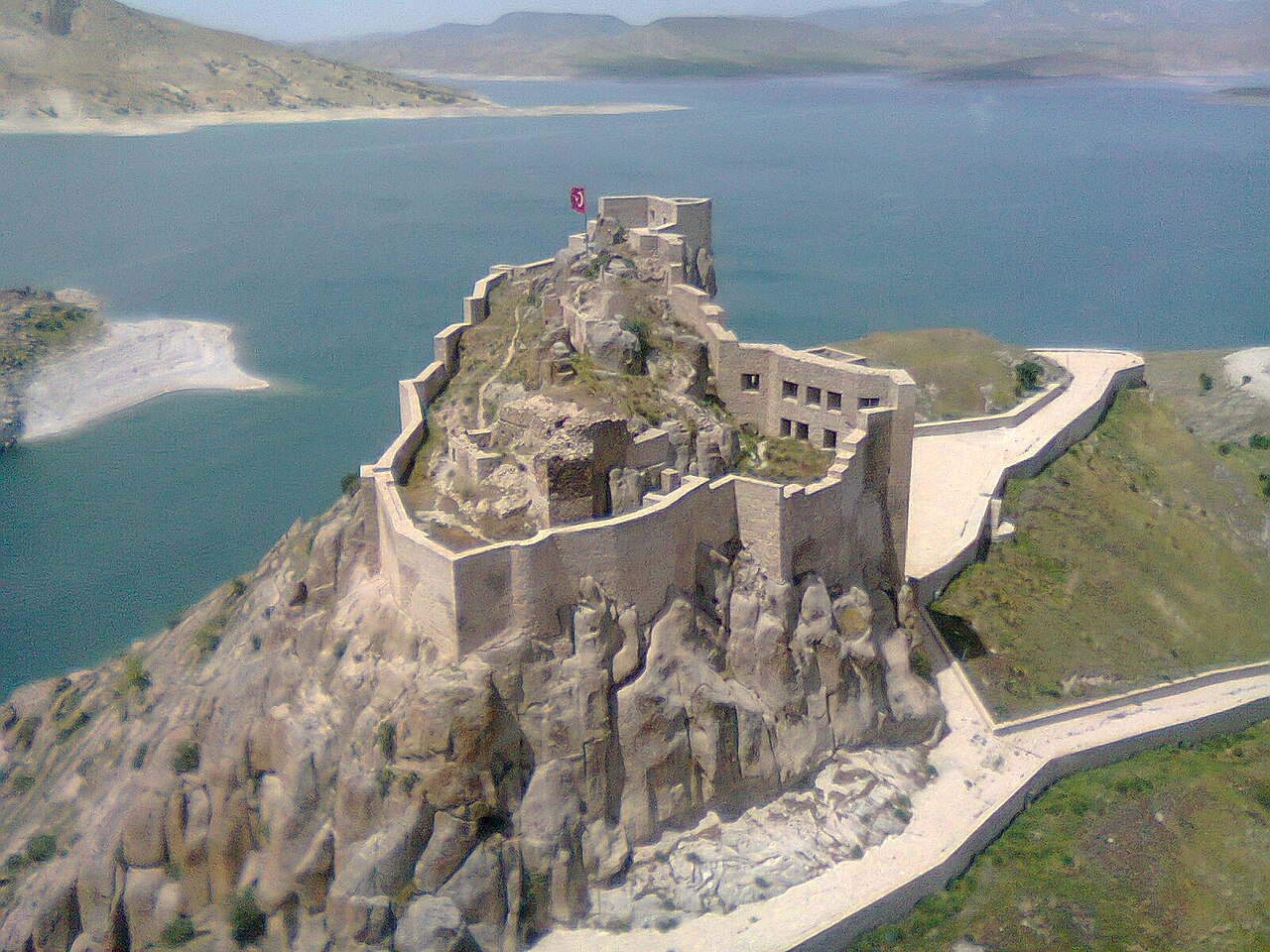 Aerial view of Pertek Castle with stone walls following a rocky ridge surrounded by blue reservoir water, May 2014