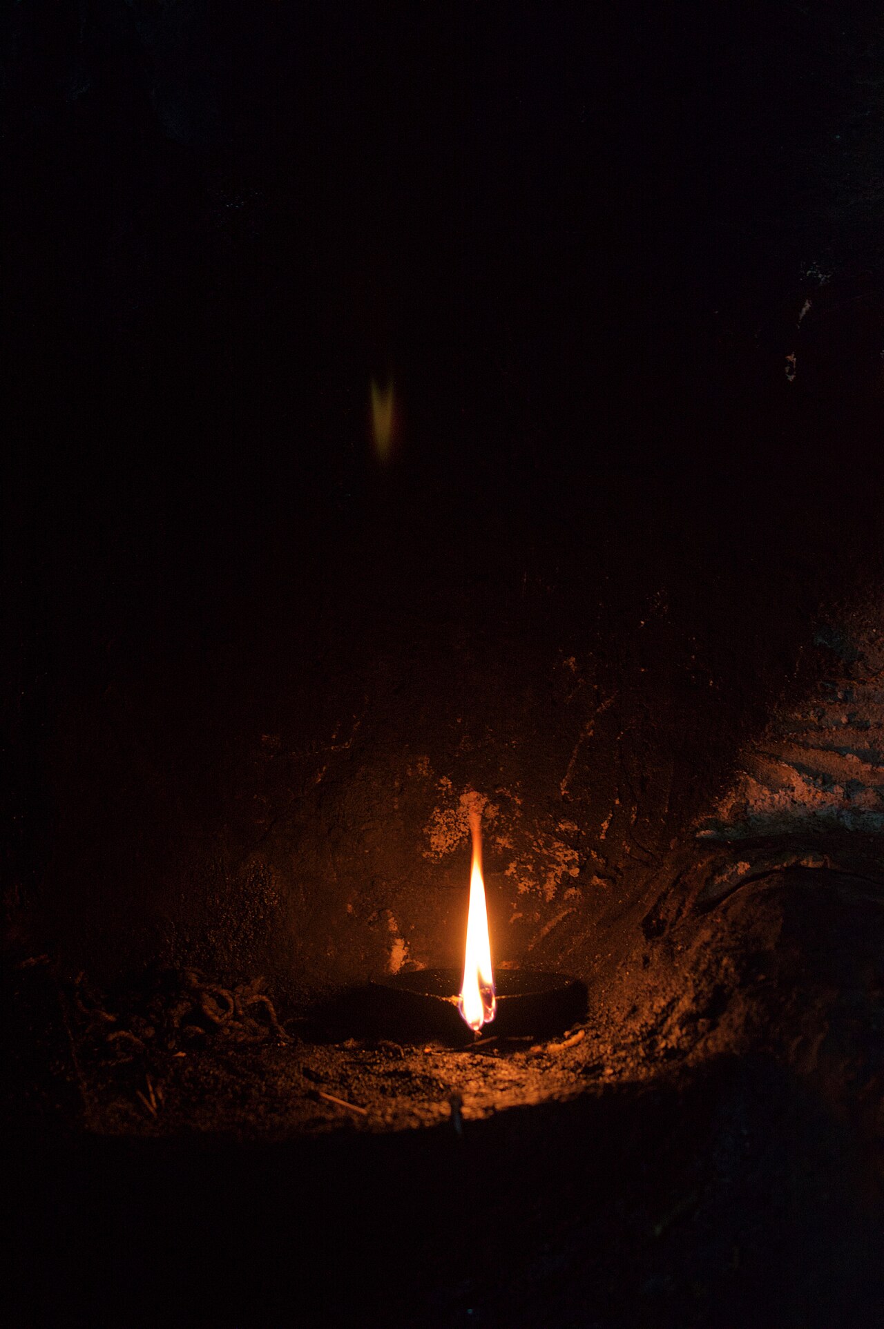 Une flamme vive brûle dans une niche de pierre sombre couverte de suie à Lalish