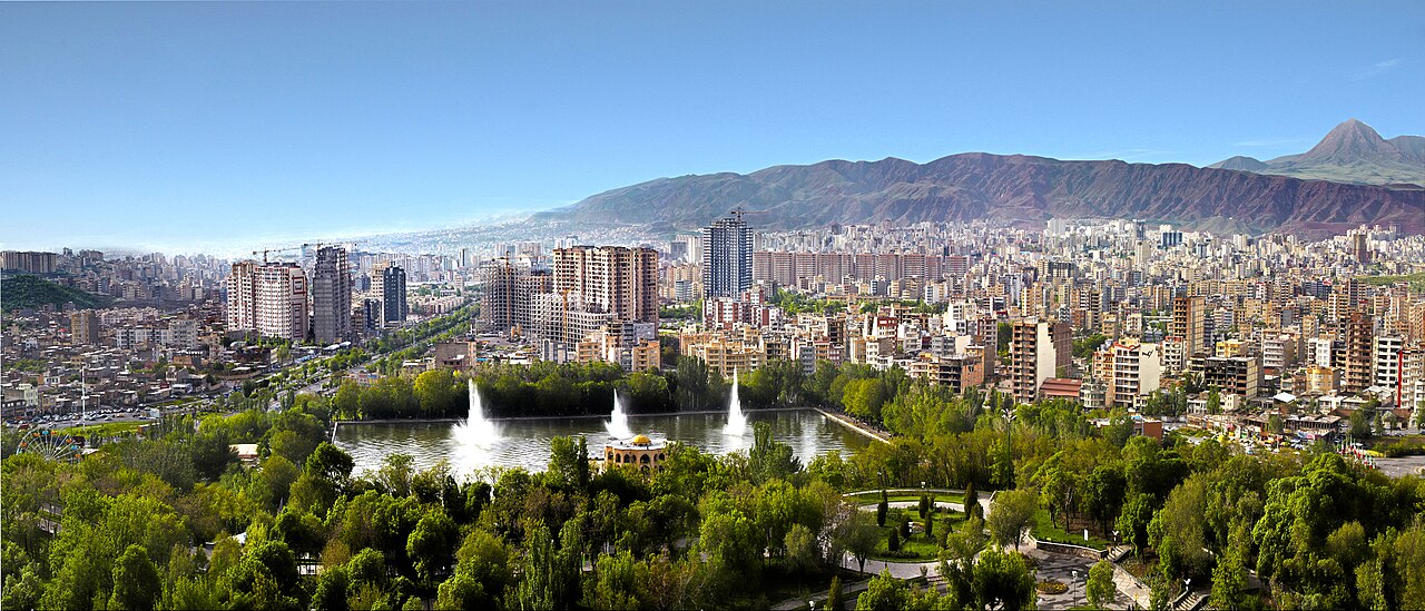 Modern Tabriz onder een bergrug, met woontorens en het boomrijke El-Goli-bassin met fonteinen op de voorgrond