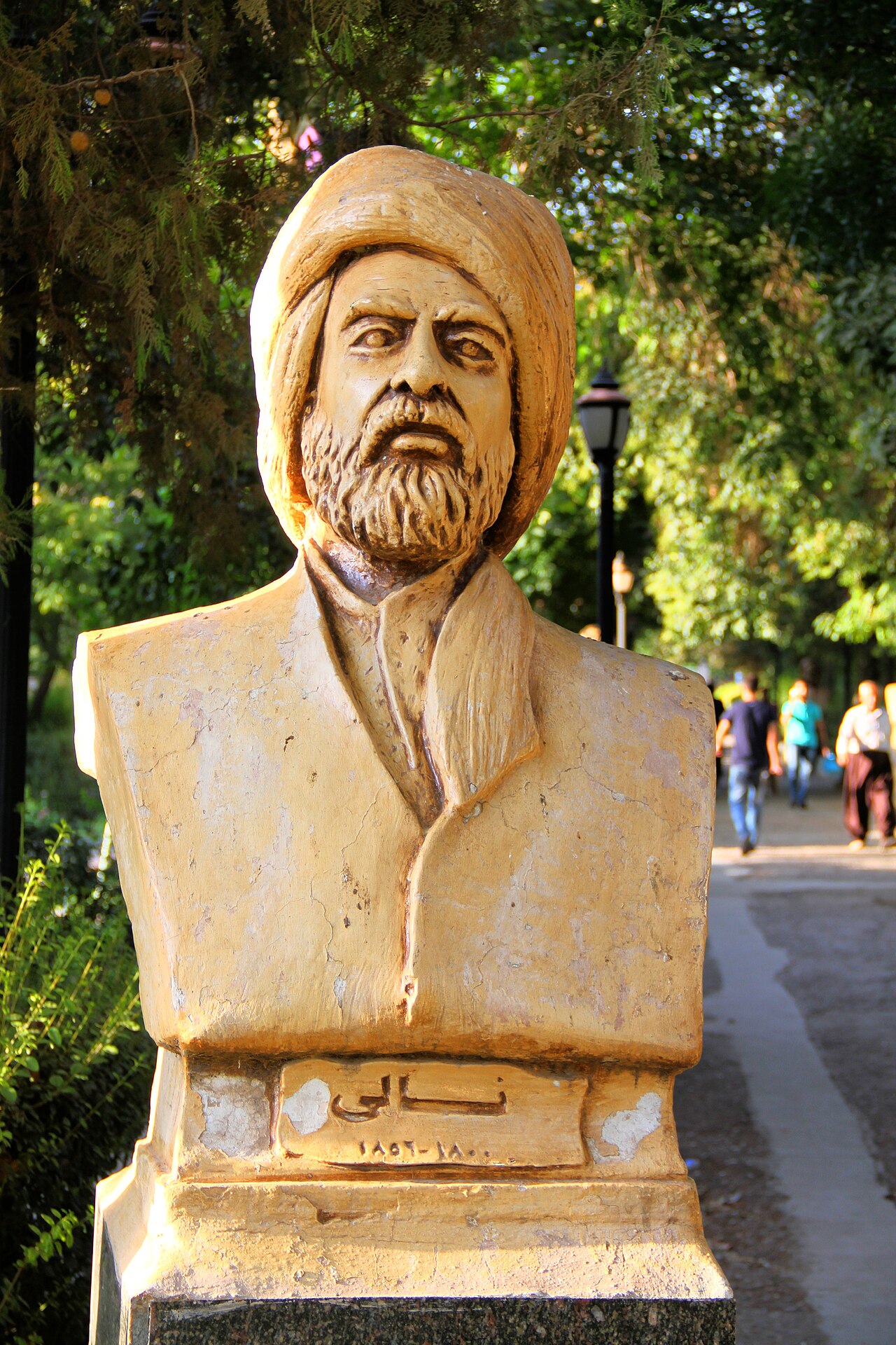Memorial bust of Nalî wearing a turban, beside a tree-lined path in Sulaymaniyah’s public garden
