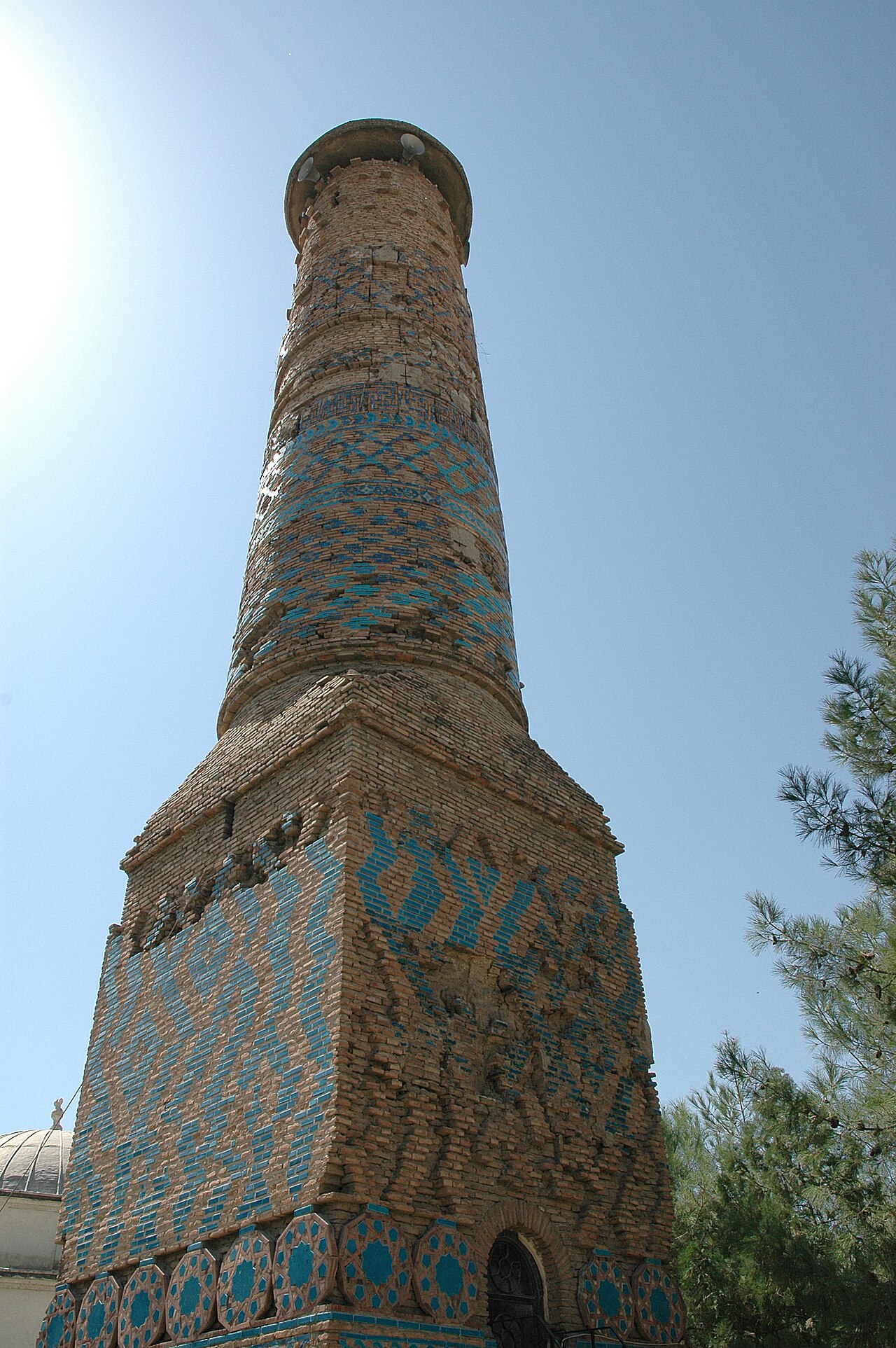 The brick minaret of Siirt’s Great Mosque, with turquoise geometric tile patterns, seen from below against a blue sky
