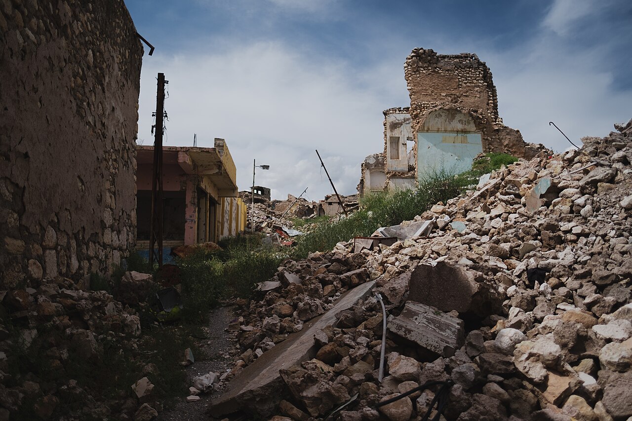 Collapsed masonry, damaged houses and vegetation along a lane in Sinjar’s old city