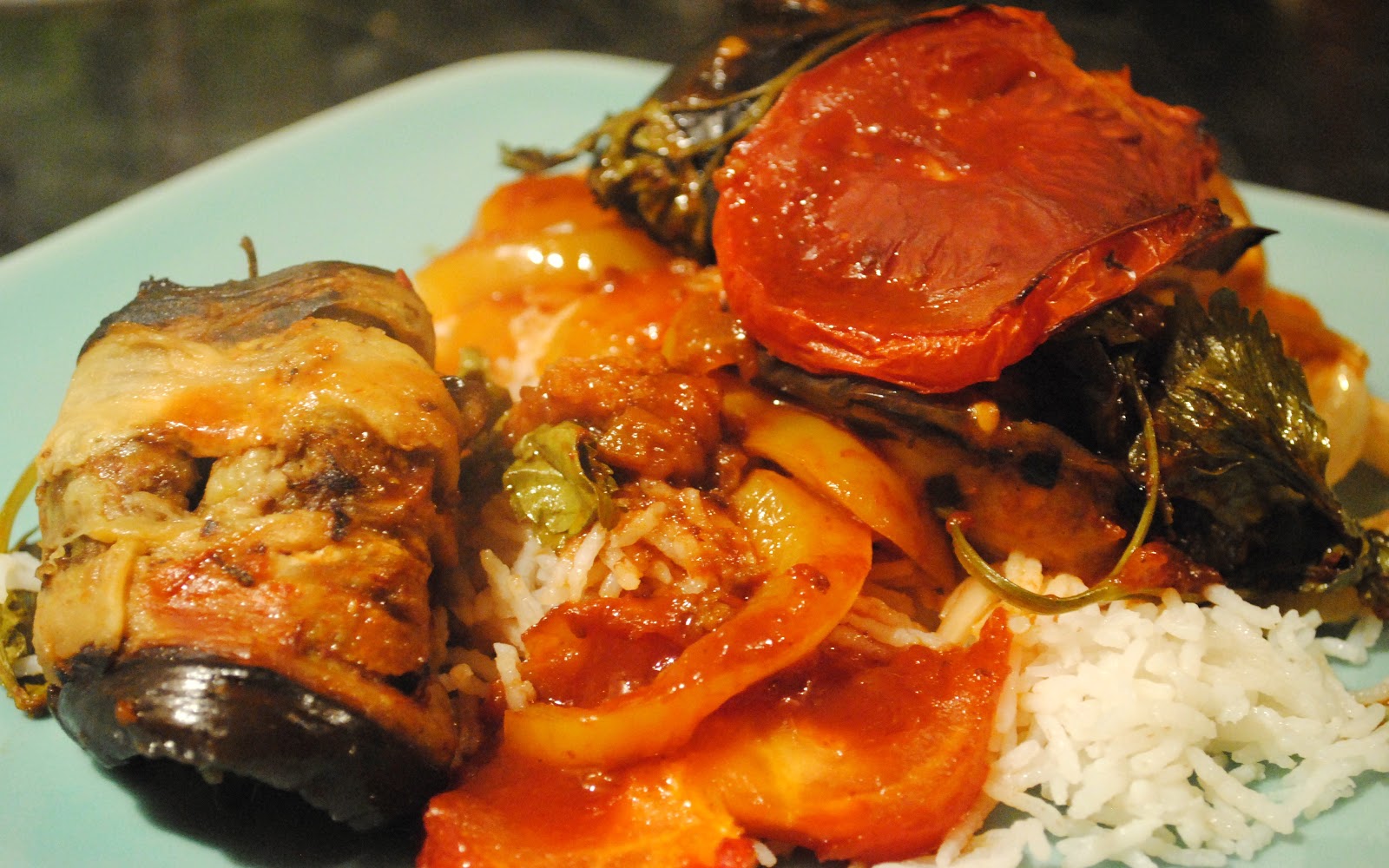 A plated serving of tepsi with aubergine, potato, roasted tomato and red sauce over white rice