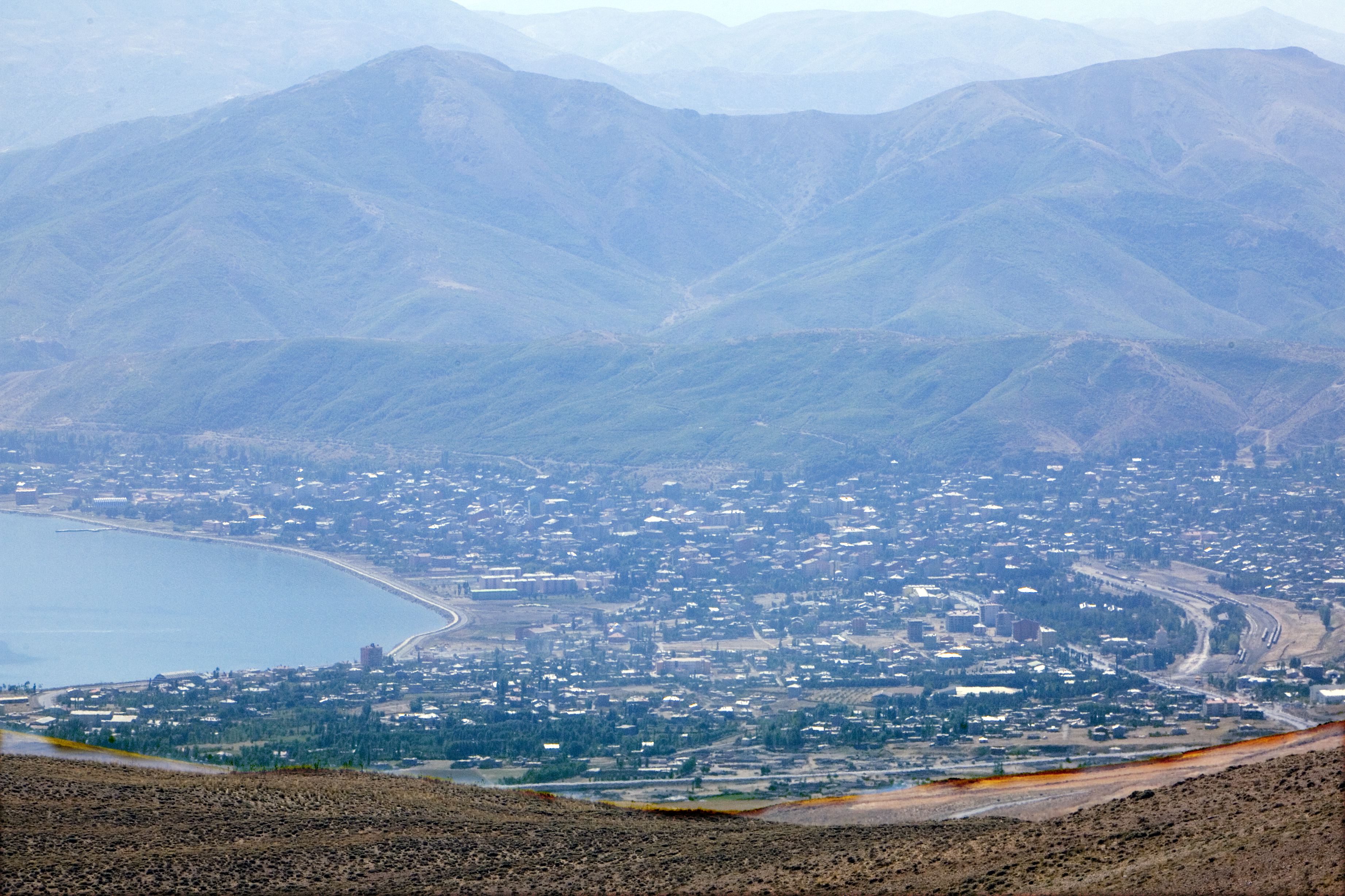 Tatvan’s buildings, curved Lake Van shoreline and railway tracks seen from the slopes of Nemrut with mountains beyond