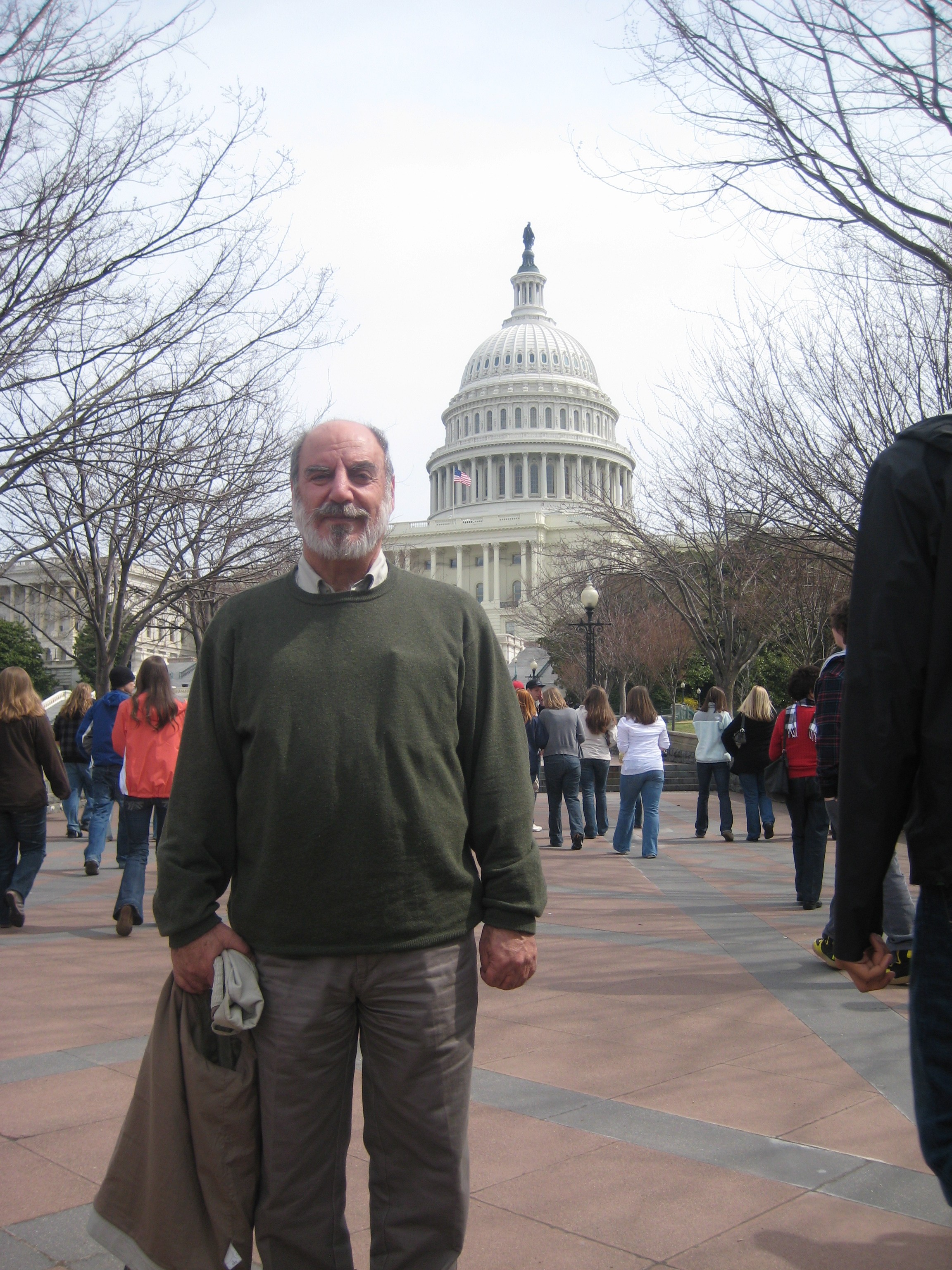 Tosinê Reşîd with a grey beard and green sweater standing in front of the United States Capitol among visitors