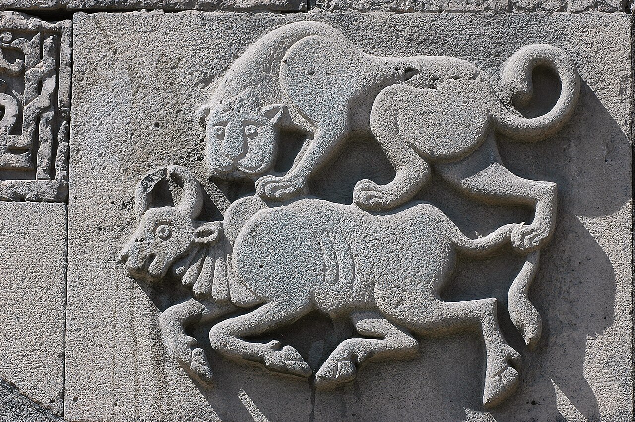 Carved stone relief at the mosque showing a lion above and attacking a horned bull, beside a fragment of Arabic inscription